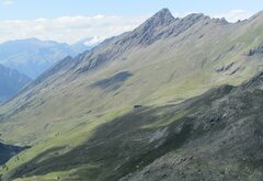 paesaggio montano con al centro un rifugio a cui giunge un sentiero. dietro la punta del Pic Traverse