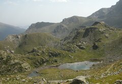 Due laghi alpini, a destra più grande e a sinistra una pozza più piccola in una conca erbosa con rocce. Intorno montagne