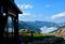 A destra, in ombra, l'ingresso del rifugio Granero con vetrata e targa in legno. Dal rifugio piccola staccionata in legno lungo il sentiero pietroso. dietro panorama montano con la catena montuosa tra le nuvole.